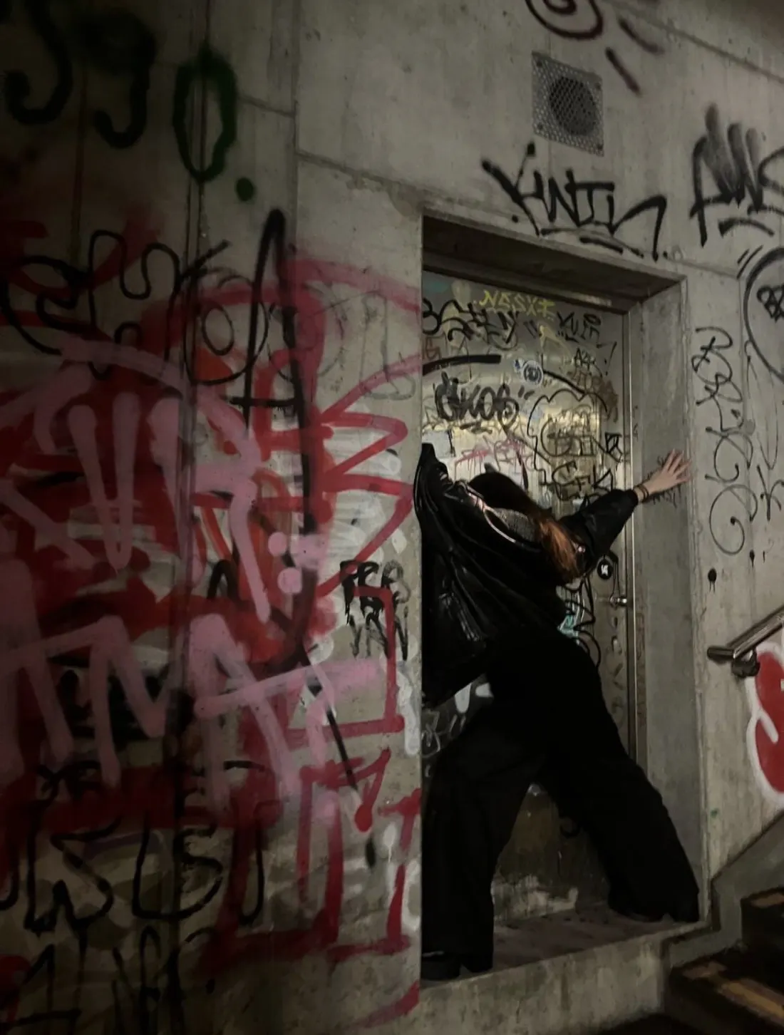 Diana in a graffiti-covered concrete doorway, arms stretched to the walls