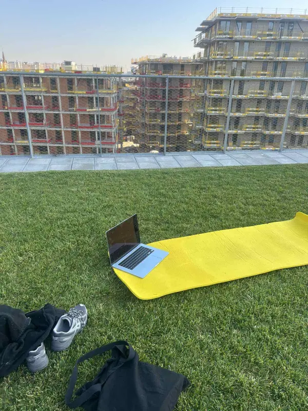 A yellow mat and a laptop on a rooftop lawn, facing buildings under construction